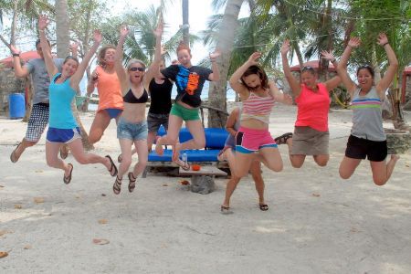 group of volunteers jumping on a beach surrounded by palm trees