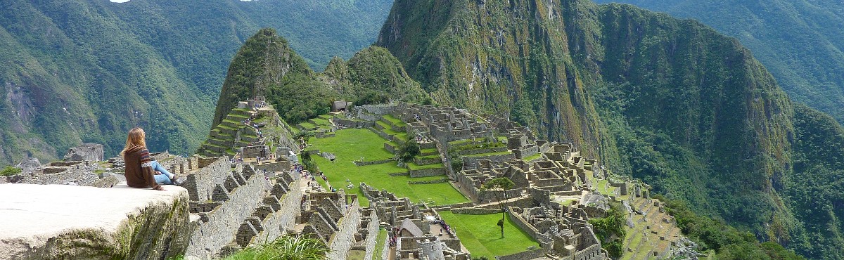 panoramic view of volunteer sitting at the edge of cliff looking down at machu picchu