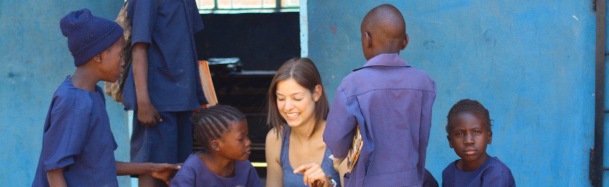 female volunteer sitting in front of school with kids group of kids