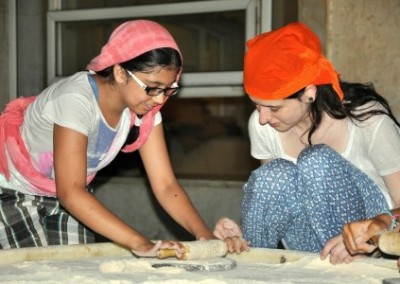 local girl showing teen volunteer how to roll pastry