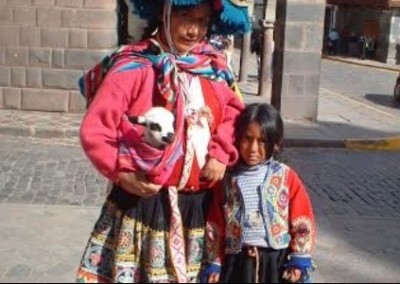 peruvian woman and girl dressed in cultural outfits with a goat wrapped in cloth