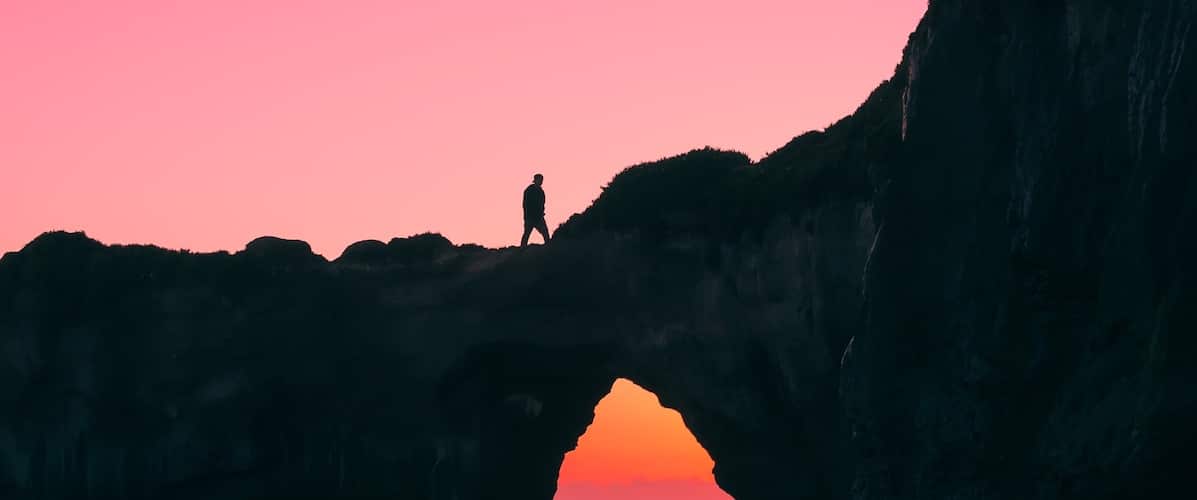 silhouette of gap year volunteer walking along beach rocks at sunset