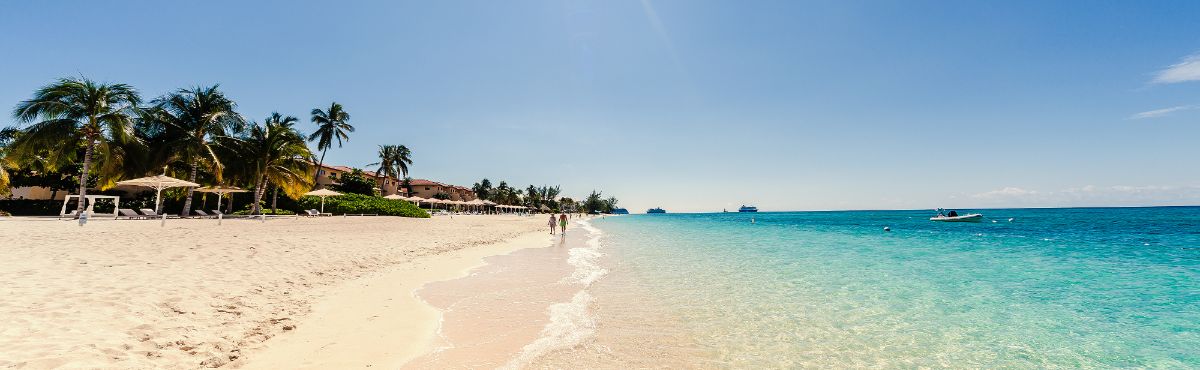 panoramic view of people walking along the white sand on little cayman beach