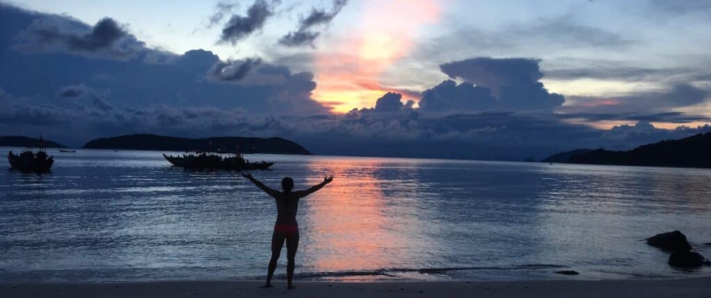 intern with hands in the air on a beach in font of the sunset