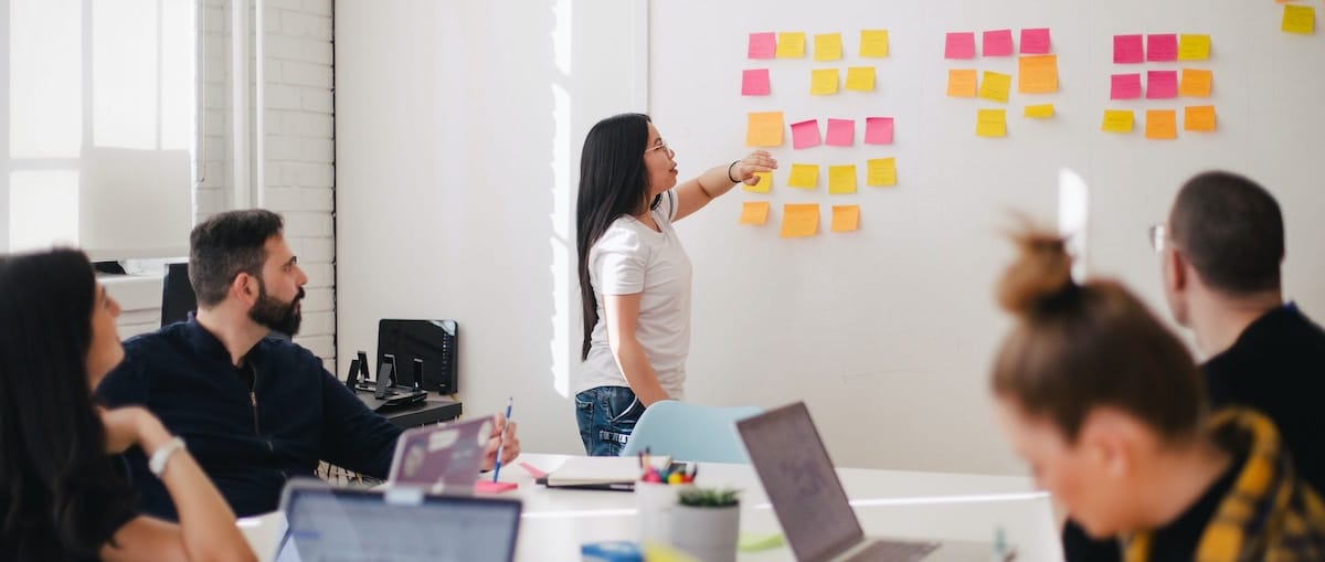 jason-goodman-Oalh2MojUuk-unsplash woman pointing to notes on a whiteboard in a meeting with interns