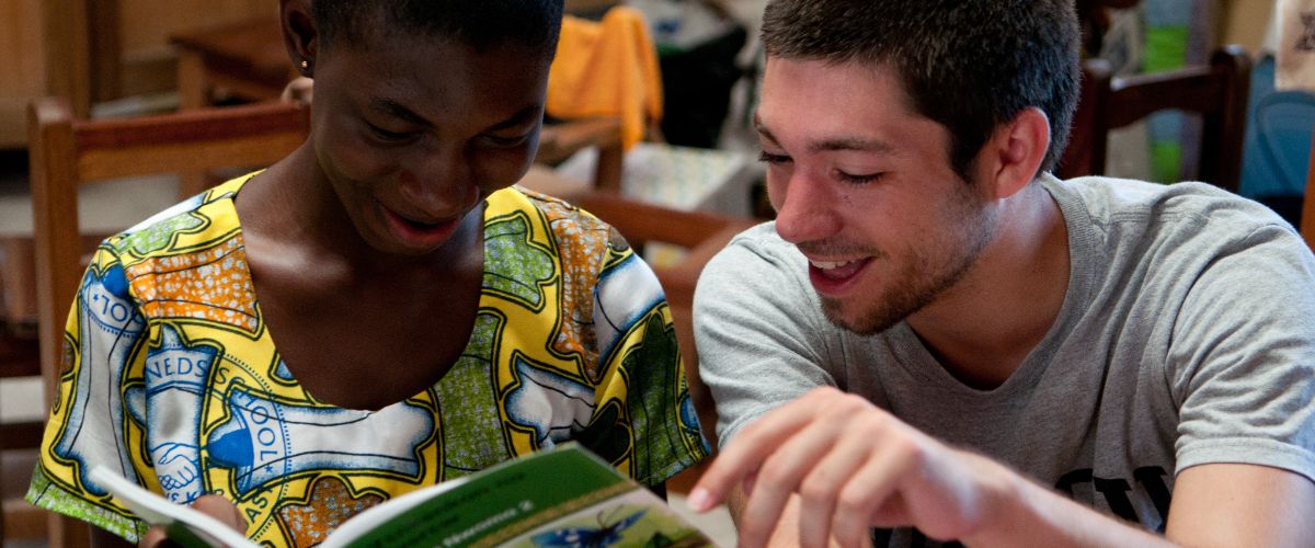 volunteer and a student sit together, smiling and reading a book